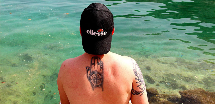 tatuaje de una brujula en la espalda de un chico en el agua